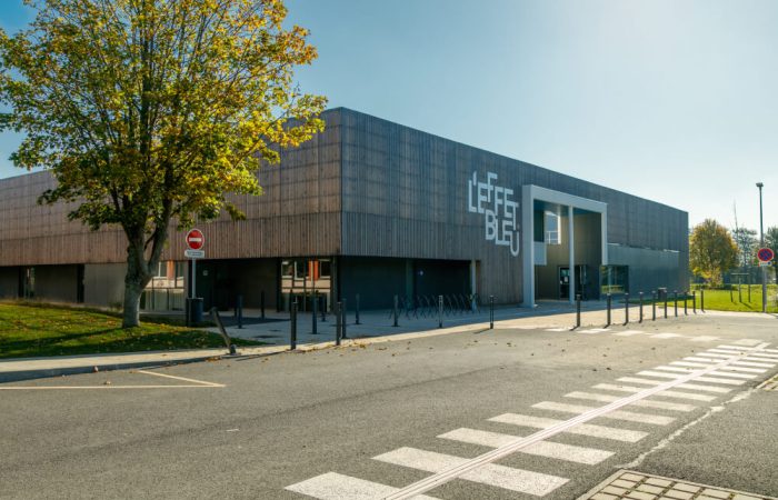 Vue de la façade urbaine du centre aquatique 'L'Effet Bleu' conçu par A26, présentant une signalétique moderne et un design architectonique avant-gardiste, aligné avec les standards de rénovation énergétique