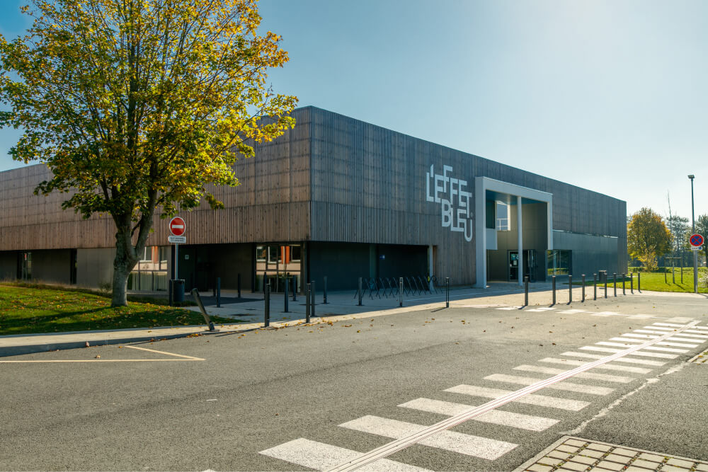 Vue de la façade urbaine du centre aquatique 'L'Effet Bleu' conçu par A26, présentant une signalétique moderne et un design architectonique avant-gardiste, aligné avec les standards de rénovation énergétique