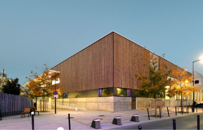 Centre aquatique durable A26 en bois avec façade en verre, intégré dans un paysage verdoyant, reflétant l'engagement envers des installations sportives écologiques et une architecture résiliente