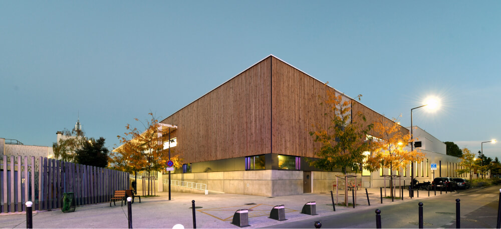 Centre aquatique durable A26 en bois avec façade en verre, intégré dans un paysage verdoyant, reflétant l'engagement envers des installations sportives écologiques et une architecture résiliente